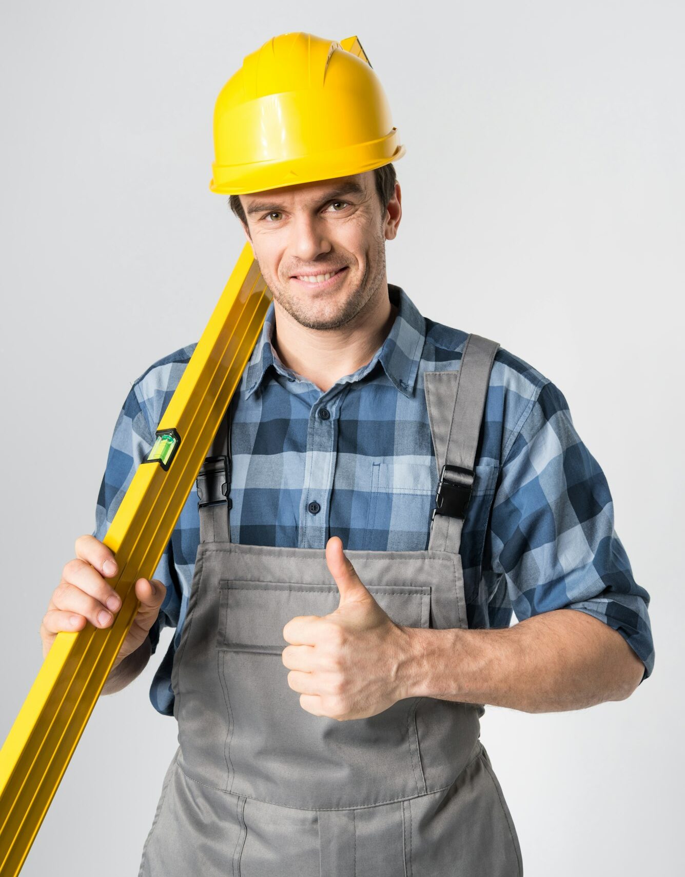 Smiling workman with level tool showing thumb up isolated on grey